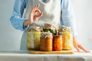 Fermented or canned vegetables, different in jars stand on the salt against the background of a woman in an apron. Processing the autumn harvest. Natural rustic style.