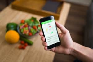 Healthy diet. Male hands holding a smartphone and keeping track of the calories of his food with a fitness app: keto meal planning apps and tools