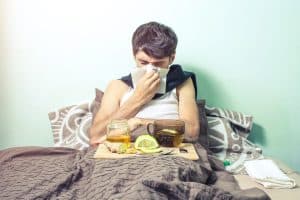 young man lies in bed sick with colds and the flu, head feels pain and suffering and treated in folk medicine, ginger, lemon, honey : symptoms of the hardest week of keto