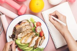 Healthy concept with nutrition food in lunch box and fitness equipments with woman writing time to get healthy on diary book : what is the keto diet?