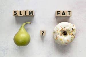 Glazed donut; pear and slim; fat text with question mark on wooden block over concrete surface: top reason why you're not losing weight on keto